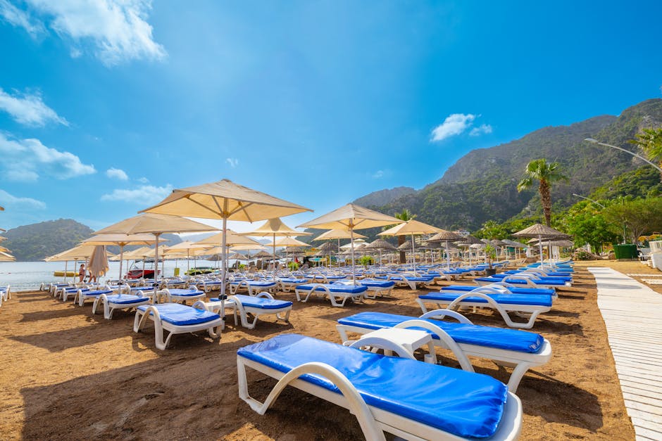 Explore the beautiful Marmaris beach with blue sunbeds and parasols under a clear sky.
